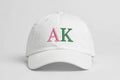 White baseball cap with AK embroidered in pink and green